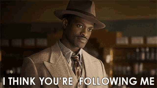 a man in a suit and hat with the words " i think you 're following me " below him