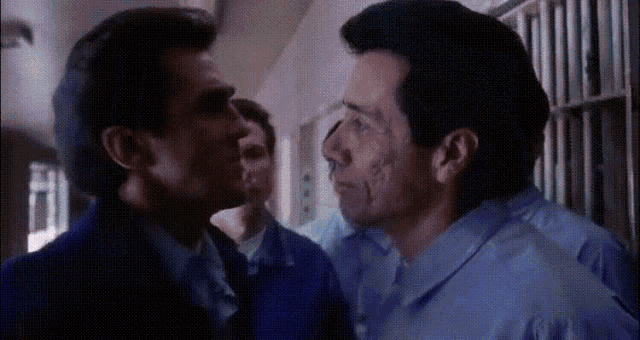 a man in a blue shirt is kissing another man in a prison cell