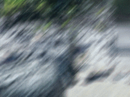 a blurred image of a waterfall with a few trees in the background