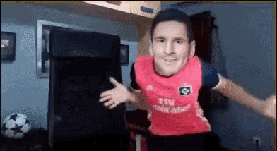 a man wearing a pink shirt with a face on it is dancing in a room .