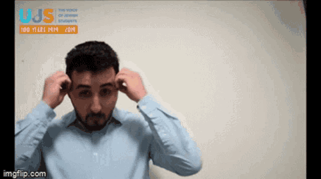 a man adjusts his ear buds in front of a sign that says ujs 100 years 1914 - 2014