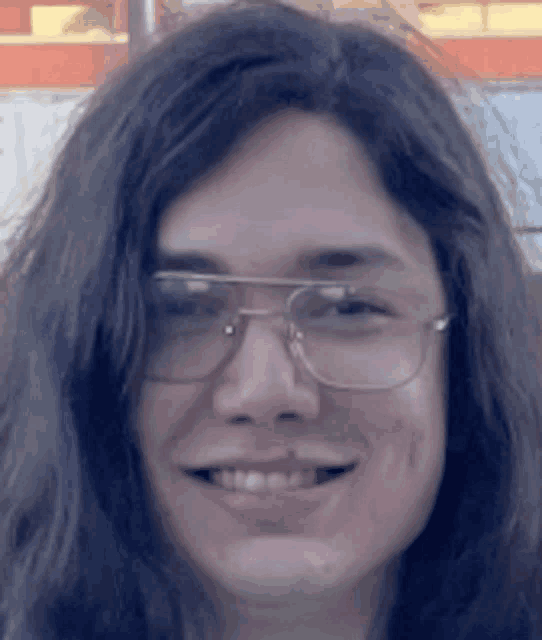 a man with long hair wearing glasses is smiling for the camera .