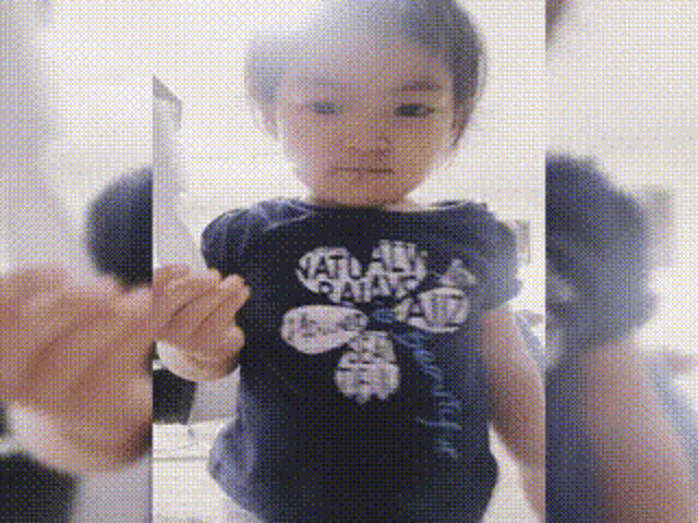 a little girl is standing in front of a mirror and looking at herself .