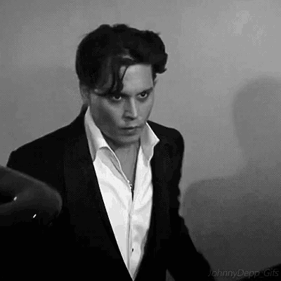 a black and white photo of a man in a suit and white shirt standing next to a hair dryer .
