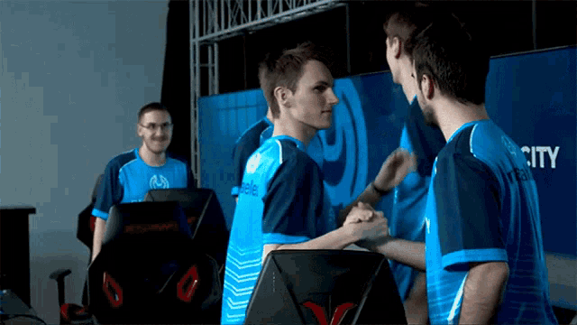 a man in a blue shirt with the word city on the back shakes hands with another man