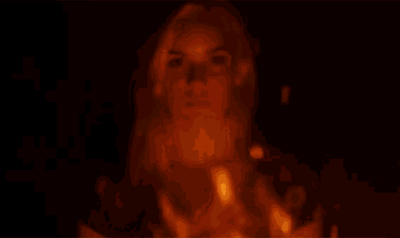 a woman is standing in front of a fire and looking at the camera .