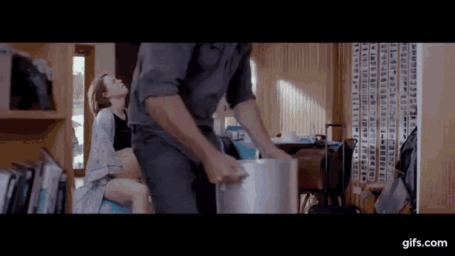 a man is holding a pot while a woman sits on a chair behind him .