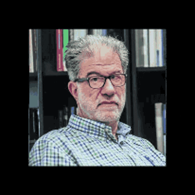 a man with glasses and a beard stands in front of a bookshelf