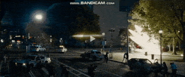 a group of people are walking down a street at night while a car is exploding in the background .