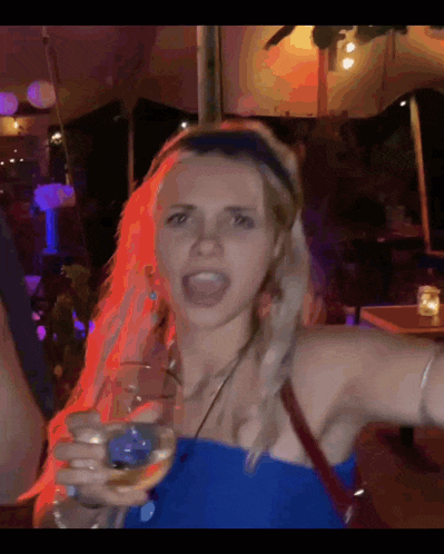 a woman in a blue top holds a glass of wine