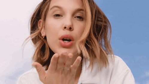 a woman blowing a kiss with her hand against a blue sky