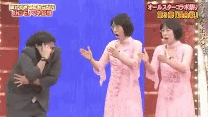 three women in pink dresses are standing next to each other on a stage in front of a blue wall .