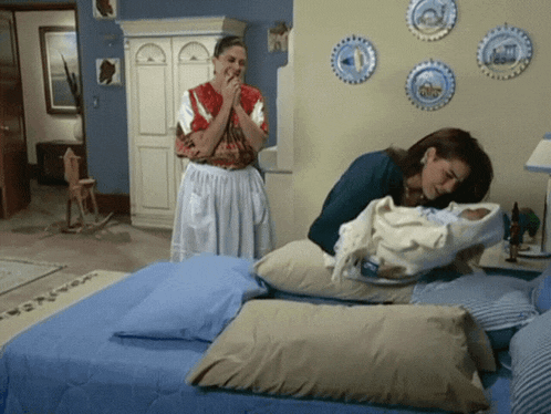 a woman holds a baby while another woman looks on in a bedroom