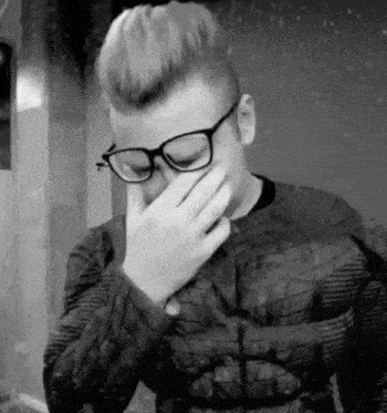a man with glasses is covering his face with his hand .