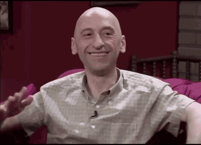 a bald man is smiling while sitting on a couch