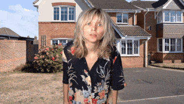 a woman in a floral shirt is standing in front of a house