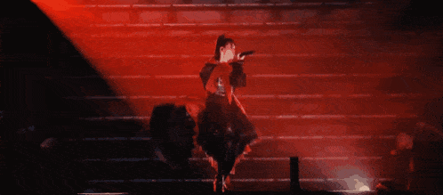 a woman in a red dress is singing into a microphone on a stage in front of a red light .
