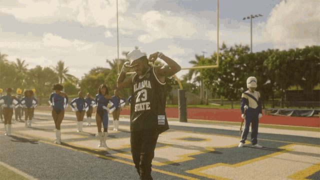 a man in an alabama state jersey stands on a field with cheerleaders