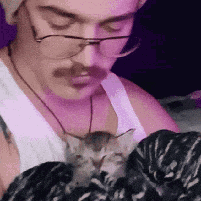 a man with glasses and a mustache is holding a kitten .