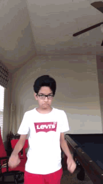 a boy wearing a white levi 's shirt and red shorts is standing in front of a pool table