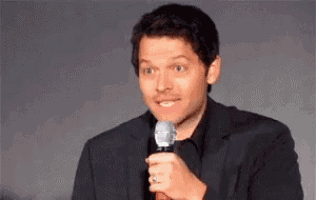 a man in a suit is holding a microphone in his hand and making a funny face .