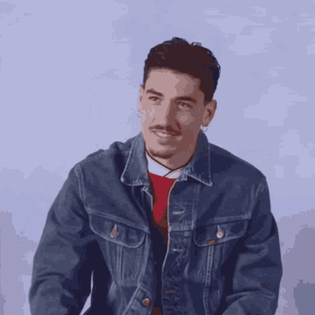 a man wearing a denim jacket is pointing up with his finger