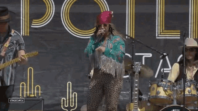 a woman singing into a microphone while a man plays a guitar and a drummer plays drums .