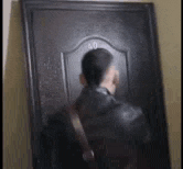 a man in a black leather jacket is looking through a door .