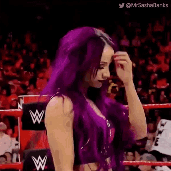 a woman with purple hair is standing in a wrestling ring in front of a crowd .