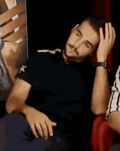 a man with a beard is sitting in a red chair with his hand on his head .