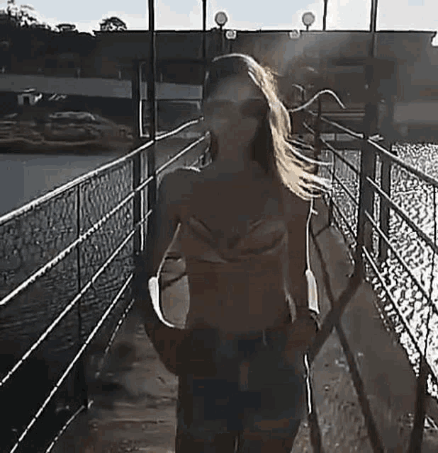a woman in a bikini and shorts is walking across a bridge over a body of water .