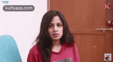 a woman in a red shirt is standing in front of a door looking at the camera .