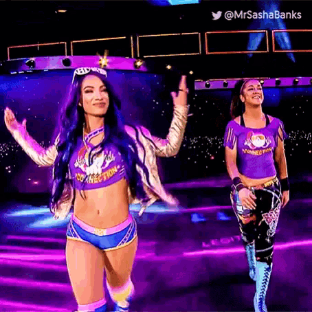two female wrestlers are walking on a stage in a purple outfit .