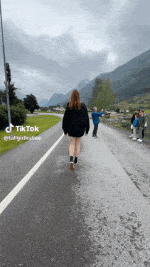 a woman walking down a road with mountains in the background has a tiktok account