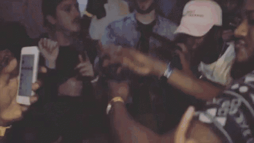 a group of people are dancing at a party and a man is holding a cell phone .