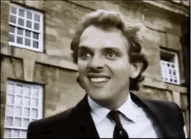 a man wearing a suit and tie is smiling in front of a building .