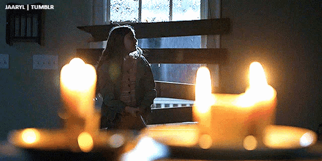 a woman standing in front of a window with candles in the foreground