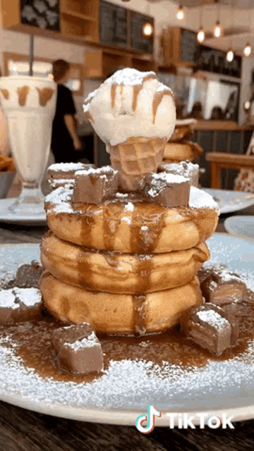 a stack of pancakes with a cone of ice cream on top and powdered sugar