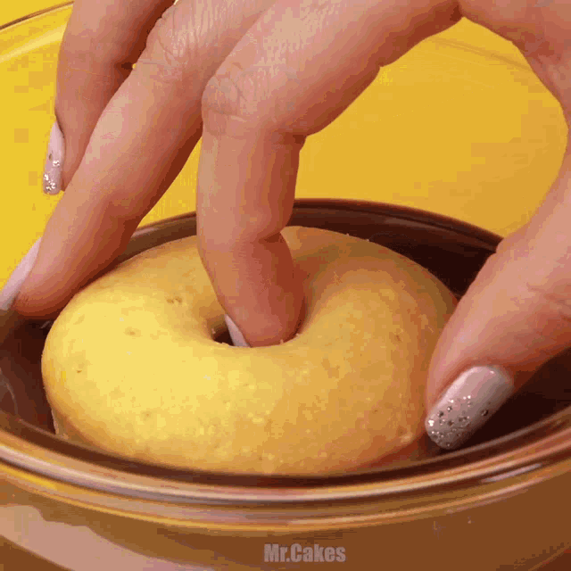 a person is putting a donut in a glass bowl with mr.cakes written on the side