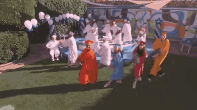 a group of people in graduation gowns are dancing in front of a pool