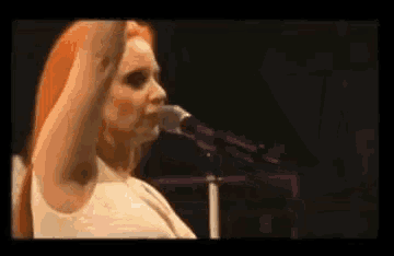 a woman with red hair is singing into a microphone while standing on a stage .