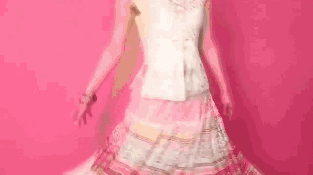 a woman in a pink dress is dancing in front of a pink wall .