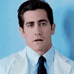 a man wearing a white lab coat and tie looks at the camera