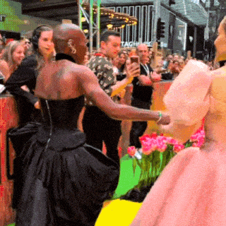 a woman in a black dress is standing in front of a crowd with a sign that says tagh on it