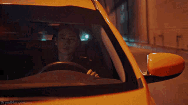 a man is driving a yellow car with the website dryedmangoez.com written on the bottom