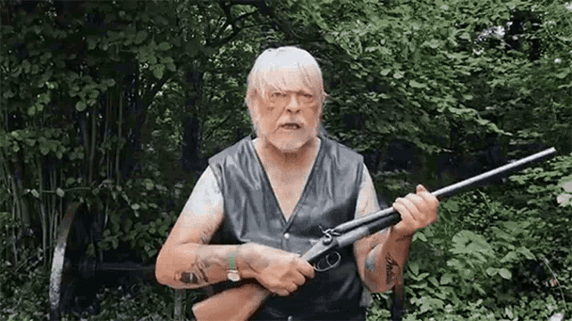 a man with a beard and tattoos is holding a shotgun in his hands .