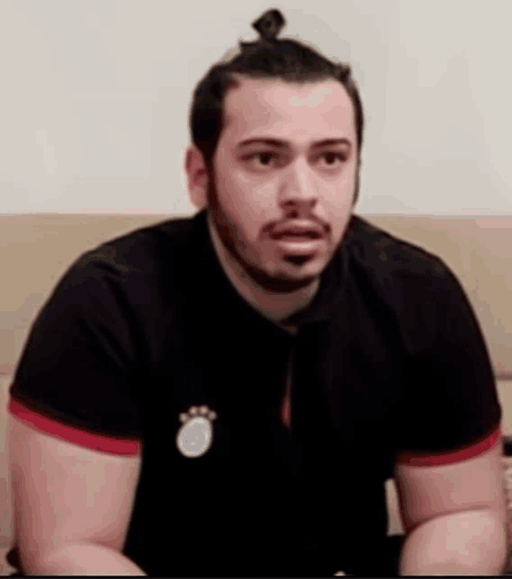 a man with a ponytail is wearing a black shirt with a white emblem on it