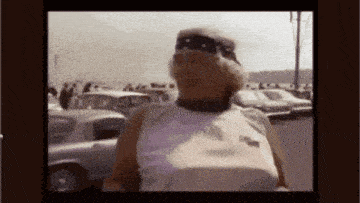 a man wearing a bandana and sunglasses is standing in a parking lot with cars