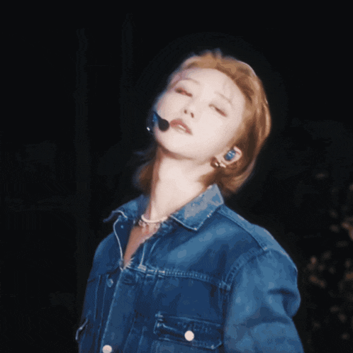 a woman wearing a denim jacket and a microphone looks up
