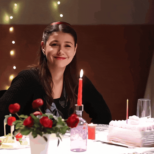 a woman sits at a table with candles and a cake